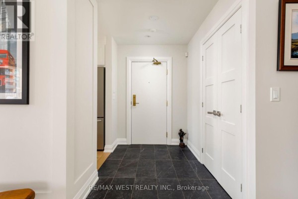 Interior hallway with dark tile flooring, white doors, and a stainless steel refrigerator. - 905 - 399 Elizabeth Street, Burlington