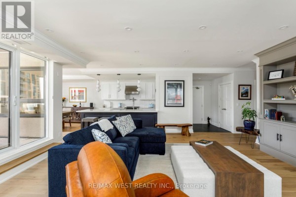 Living room with navy sectional, leather chair, and open-concept kitchen with island. - 905 - 399 Elizabeth Street, Burlington