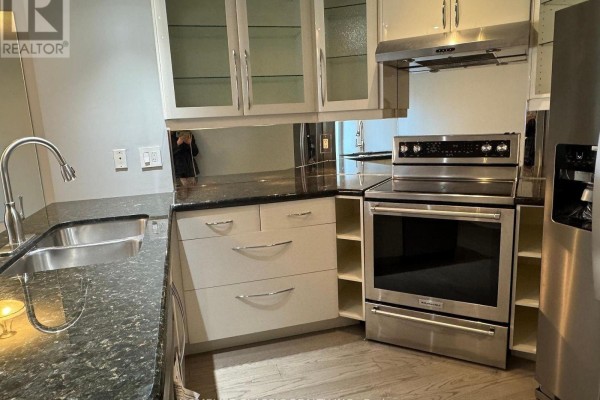 Close-up of a kitchen counter with a stainless steel sink, faucet, granite countertop, and white cabinets. - 905 - 909 Bay Street, Toronto
