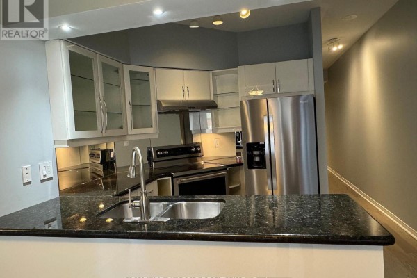 View of a kitchen with a stainless steel refrigerator, stove, cabinets, and a granite countertop island. - 905 - 909 Bay Street, Toronto