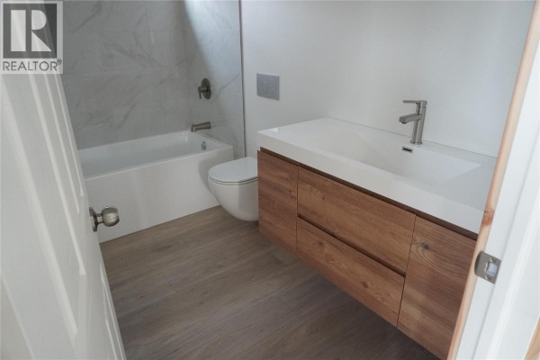 Modern bathroom with a floating vanity, white tub, and marble tile. - 905 13 Avenue S, Golden