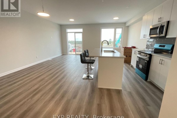 Open-concept living and kitchen area with light wood flooring, white cabinets, and a large island with seating. - 905 Jack Dalgity Street, Mississippi Mills