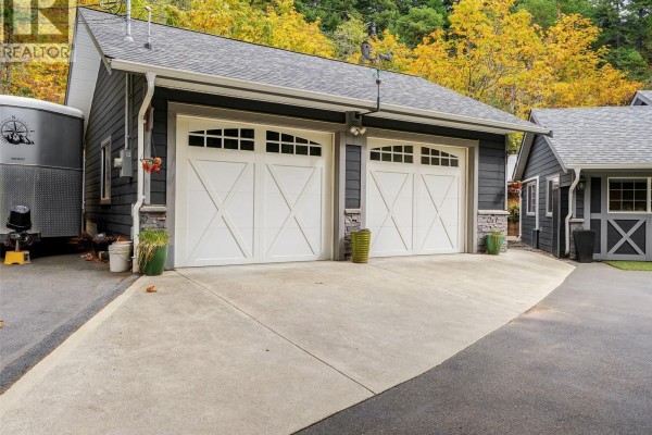 Double detached garage with white doors, grey siding, and stone accents. - 905 Worrall Dr, Langford