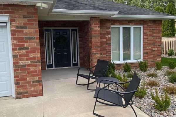 Close-up of the front entrance with a black door, sidelights, and two rocking chairs on the porch. - 9053 Indian Creek Line E, Chatham Kent