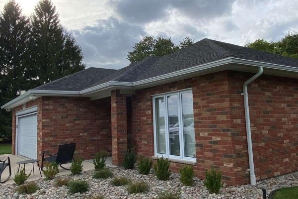Exterior view of the brick house showcasing the roofline, white gutters, and a large window. - 9053 Indian Creek Line E, Chatham Kent