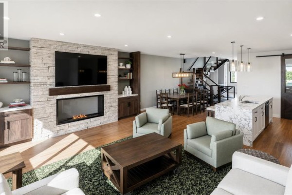 Living room with stone fireplace, large television, dining area, and kitchen island. - 905a Bridge Road, Canmore