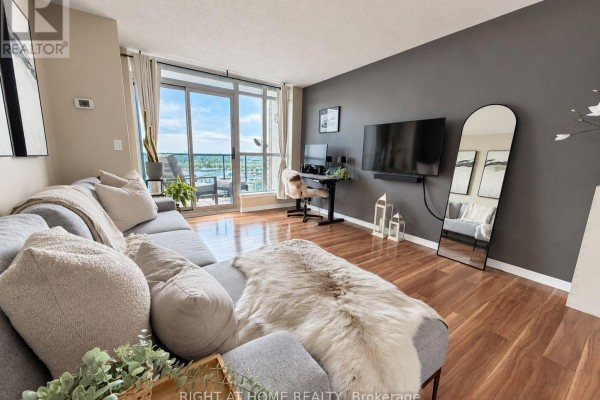 Living room with a gray sofa, large window, and a view of the water. - 906 - 340 Watson Street W, Whitby