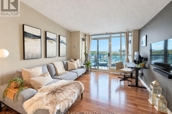 Living area with a gray sectional sofa, hardwood floors, and a balcony view. - 906 - 340 Watson Street W, Whitby