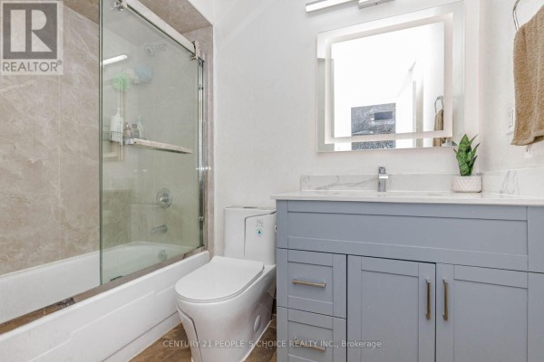 A bathroom with a grey vanity, white toilet, and a bathtub with a glass sliding door. - 906 - 3577 Derry Road E, Mississauga
