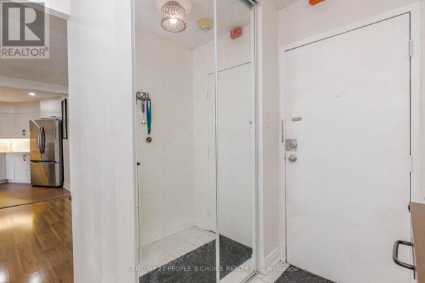 An apartment entrance with a white door, mirrored closet, and wood-look flooring. - 906 - 3577 Derry Road E, Mississauga