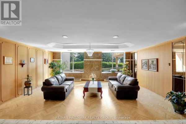 Lobby seating area with two dark leather sofas, a coffee table, and wood paneling. - 906 - 960 Teron Road, Ottawa