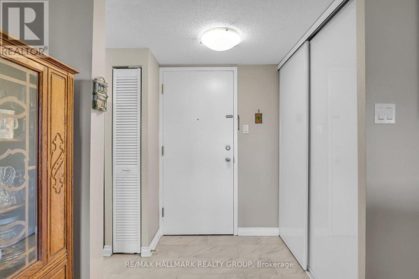 Apartment entryway with a white door, a mirrored closet, and light beige walls. - 906 - 960 Teron Road, Ottawa