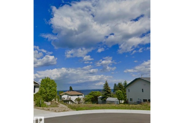 View of a vacant lot with houses on either side, and a distant view of a lake under a cloudy sky. - 906 26 St, Cold Lake
