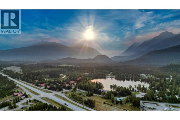 Aerial view of a wide valley with a highway, lake, and tree-covered mountains under a bright sun. - 906 Harrwood Drive, Blue River