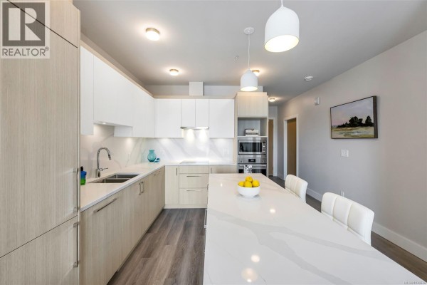 L-shaped kitchen featuring light wood cabinets, white quartz counters, and stainless steel appliances. - 907 622 Admirals Rd, Esquimalt