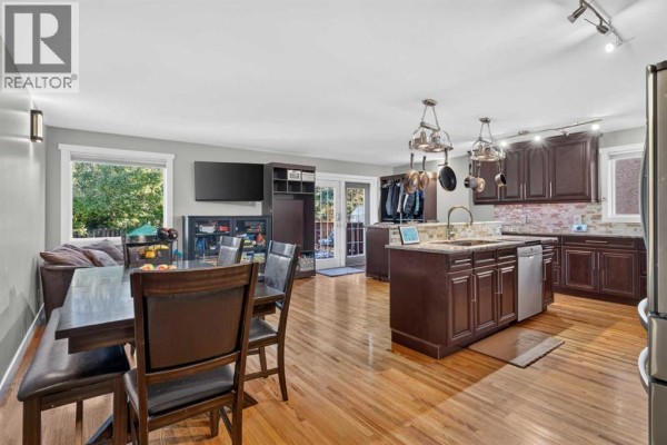 Open concept living and dining area adjacent to a kitchen with dark wood cabinets. - 907 Ranchview Crescent Nw, Calgary