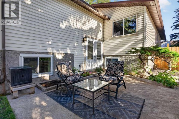 Close-up of a patio with seating area and a glass-top table next to the house. - 907 Ranchview Crescent Nw, Calgary