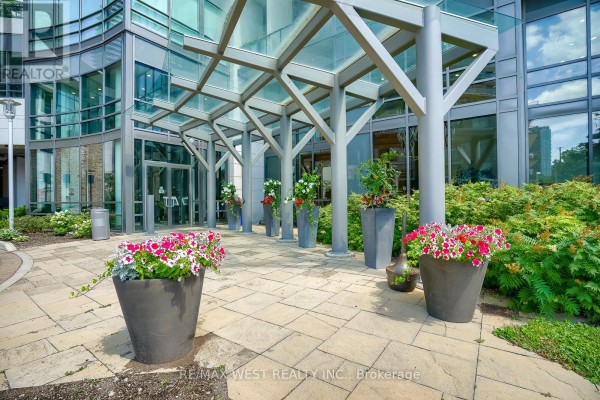 Entrance to building with glass canopy, stone pavers, and potted flowers. - 908 - 2240 Lake Shore Boulevard W, Toronto