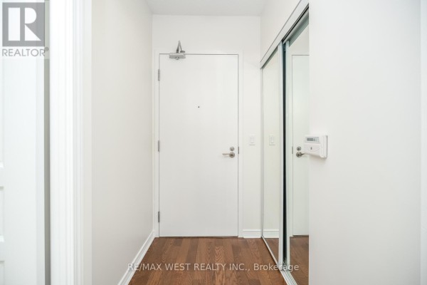 Hallway with white door, hardwood floor, and mirrored closet doors. - 908 - 2240 Lake Shore Boulevard W, Toronto