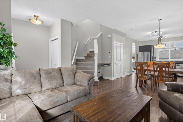 View from living room showing a sectional sofa, stairs, and adjacent dining area with kitchen. - 9082 Rosenthal Link Li Nw, Edmonton