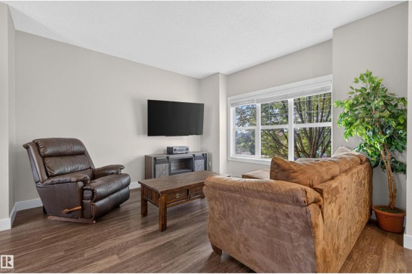 Living room with a brown leather recliner, sectional sofa, coffee table, and a large window. - 9082 Rosenthal Link Li Nw, Edmonton