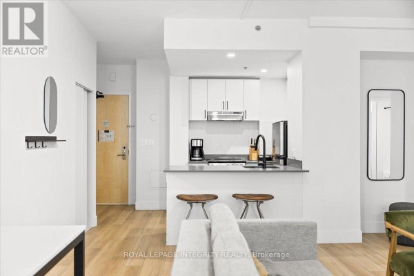 Apartment kitchen with white cabinetry, stainless steel appliances, island, and two stools. - 909 - 161 Laurier Avenue W, Ottawa