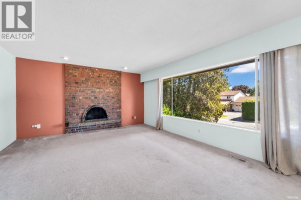 Living room with large window, brick fireplace, and sliding glass door to balcony. - 9091 Ash Street, Richmond