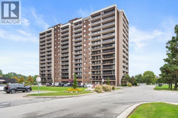 Exterior view of a brick apartment building with multiple balconies under a blue sky. - 9099 Riverside Drive East Unit# 907, Windsor