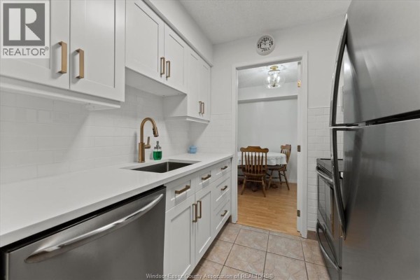 White kitchen with stainless steel appliances, gold faucet, subway tile backsplash, and a glass-paned door. - 9099 Riverside Drive East Unit# 907, Windsor