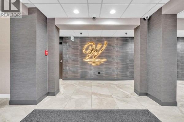 Hallway with textured grey walls, a lit sign, and tiled floors leading to an elevator. - 9099 Riverside Unit# 402, Windsor