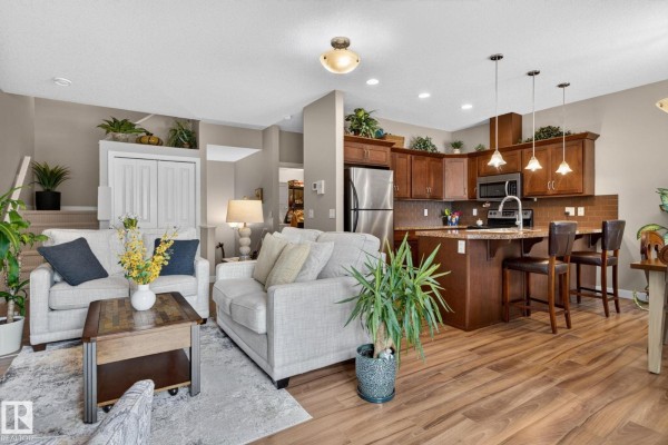 Open-concept living room and kitchen with light beige sofas, dark wood cabinets, and granite countertops. - #91 7293 South Terwillegar Dr Nw, Edmonton