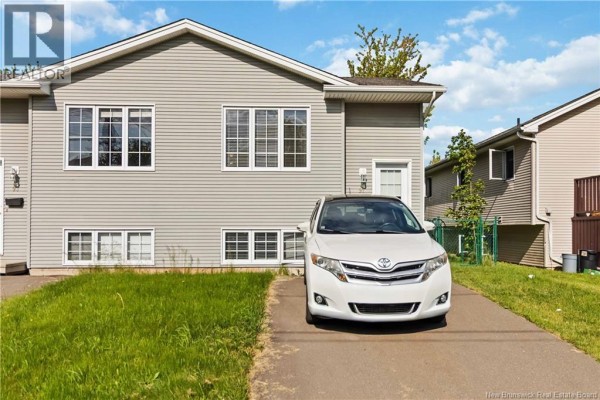 Side exterior of a duplex with beige vinyl siding, featuring a white SUV parked in the driveway. - 91-93 Second Avenue, Moncton