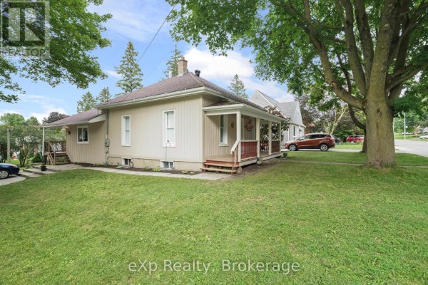 Side exterior of the light yellow house with a porch and green lawn in the foreground. - 91 Charles Street, North Huron