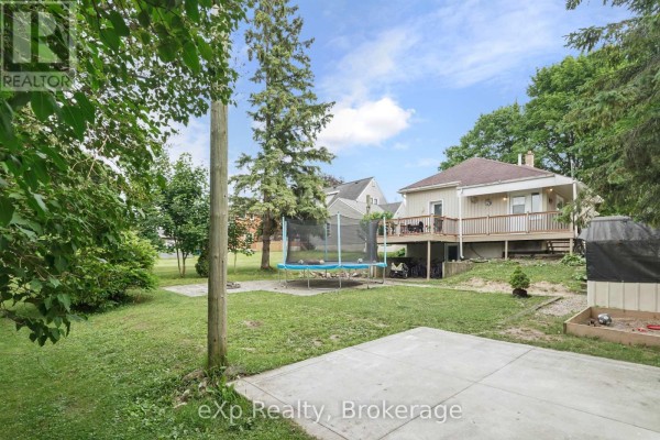 Backyard view of the light yellow house with a wooden deck, trampoline, and concrete patio area. - 91 Charles Street, North Huron