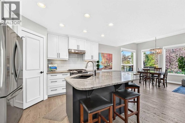 Kitchen island with granite countertops and dark cabinetry, white cabinets, stainless steel appliances, and hardwood floors. - 91 Cranfield Circle Se, Calgary
