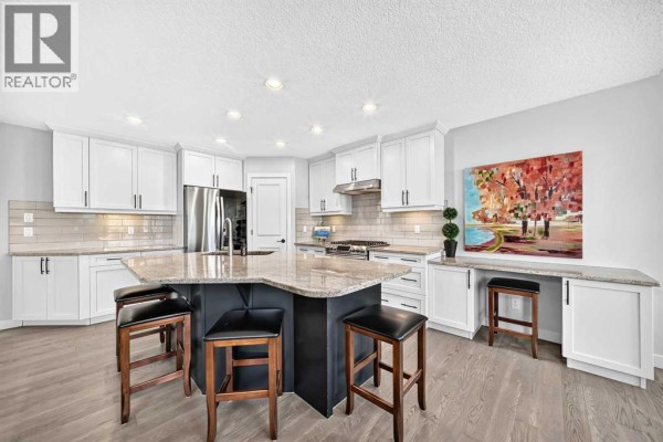 View of the kitchen island and white cabinetry, with a built-in desk area and hardwood floors. - 91 Cranfield Circle Se, Calgary