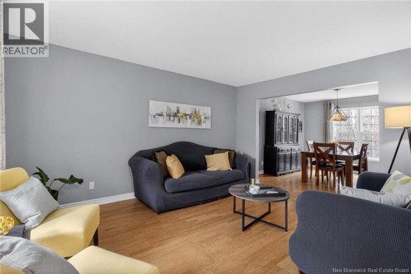 Living room with gray walls, hardwood floors, a dark blue sofa, and yellow accent chairs. - 91 Greenwich Drive, Moncton