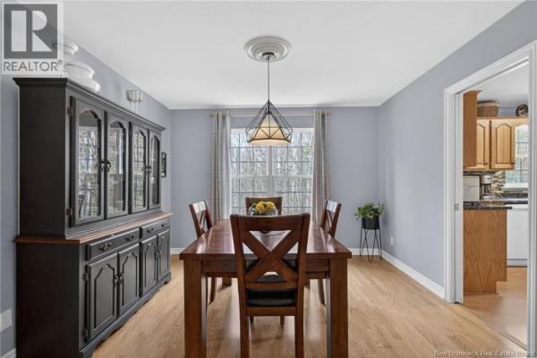 Dining room with a wooden table and chairs, a dark hutch, and a window view. - 91 Greenwich Drive, Moncton
