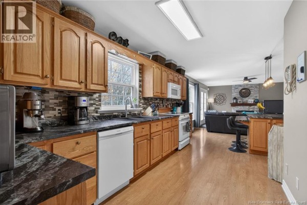 Kitchen with light wood cabinets, granite countertops, a dishwasher, and an open doorway to the living area. - 91 Greenwich Drive, Moncton