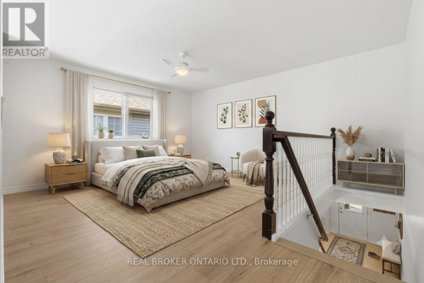 A bright bedroom with a king-size bed, wood flooring, and a staircase with dark banister. - 91 Lynch Circle E, Guelph