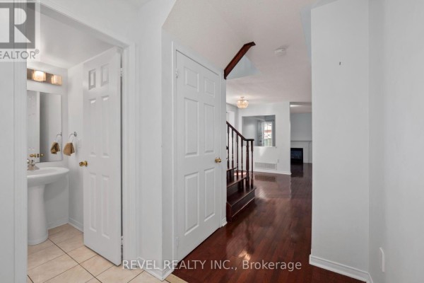 Interior hallway with white doors, pedestal sink in a small bathroom, and dark wood staircase. - 91 Oceanpearl Crescent, Whitby