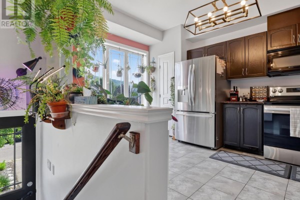 Kitchen island with plants, stainless steel refrigerator, dark cabinets, and tiled flooring visible. - 91 Willow Lane, Grimsby