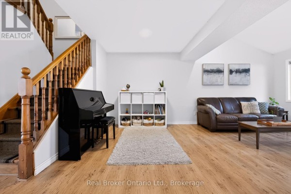 Living room with a brown leather sofa, coffee table, white storage unit, black upright piano, and wood-look flooring. - 91 York Street E, Centre Wellington