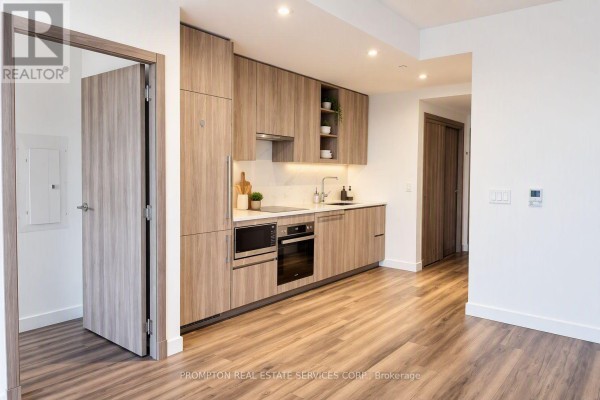 Contemporary kitchen with light wood cabinetry, stainless steel appliances, and quartz countertops with a wooden floor. - 911 - 25 Mcmahon Drive, Toronto