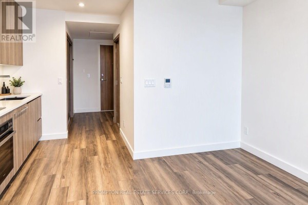 View of an empty living space with white walls and wood flooring, adjacent to a hallway with wood doors. - 911 - 25 Mcmahon Drive, Toronto