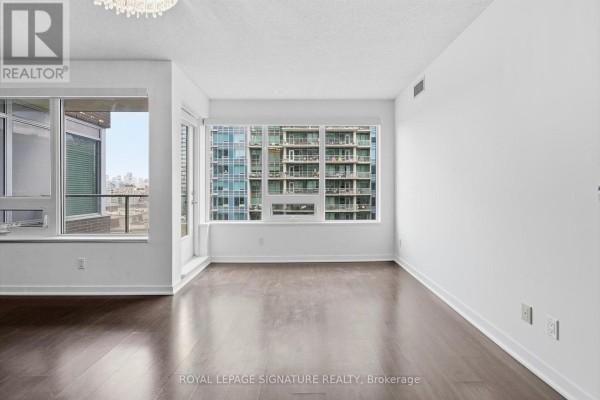 Bright living room with dark hardwood floors and a large window overlooking an urban landscape. - 911 - 59 East Liberty Street, Toronto