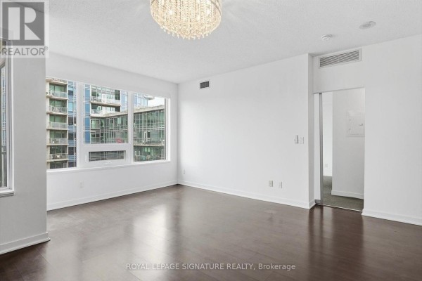 Spacious living room with dark hardwood floors, white walls, and a window view of adjacent building. - 911 - 59 East Liberty Street, Toronto