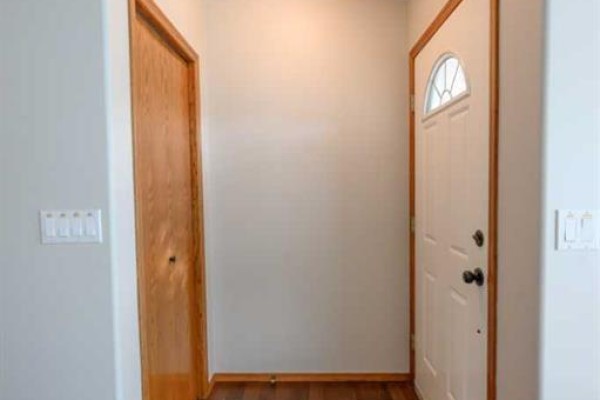 Interior view of a doorway, showing a white front door and a wooden closet door. - 9114 110a Avenue, Grande Prairie