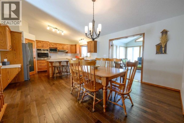 Dining area and kitchen with wood cabinets, a large wooden table, and light-colored countertops. - 9114 110a Avenue, Grande Prairie