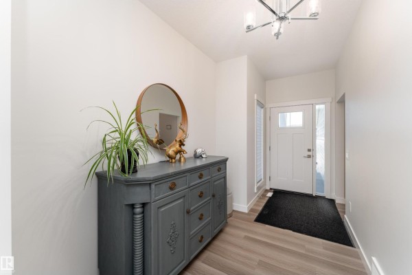 Foyer with grey sideboard, staircase, and view into the kitchen with island and bar stools. - 9119 183 Av Nw, Edmonton